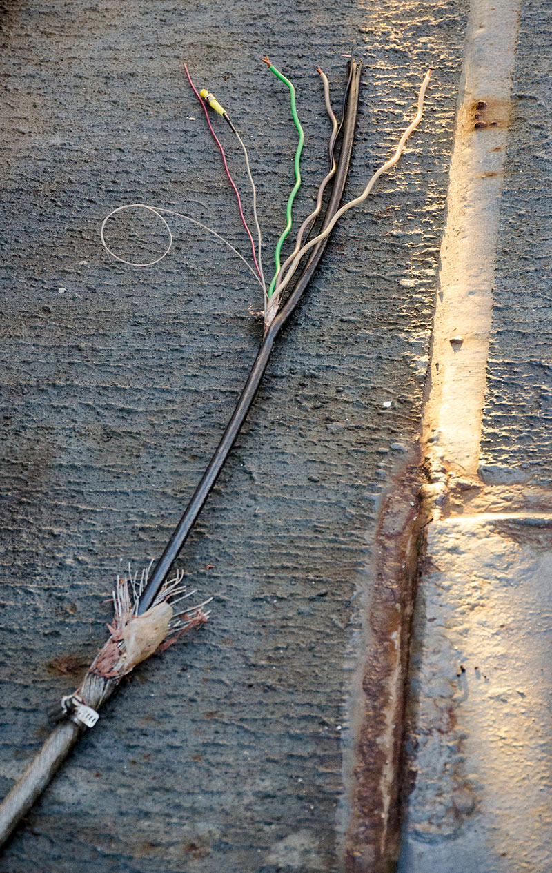 Image showing the first cut of the .68 cable, at 2,700 meters (8,858 feet). The three layers of steel are peeled back to expose the black core containing three electrical conductors (brown and green twisted), three fibers (black, red, and white with yellow end), and drain wire (curled white). The Fiber Response Team performed a quick termination on one fiber and confirmed that the short was an additional 150 meters (492 feet) up the cable. 
