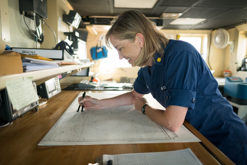 LCDR Fionna Matheson plots fixes on the paper charts on the bridge of NOAA Ship Okeanos Explorer.