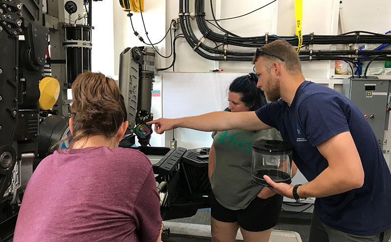 Chris Ritter, Global Foundation for Ocean Exploration Operations Manager for Leg 2 of the expedition, gives a tour of the remotely operated vehicles to Windows to the Deep 2019 Science Leads Amy Wagner and Alexis Weinnig.