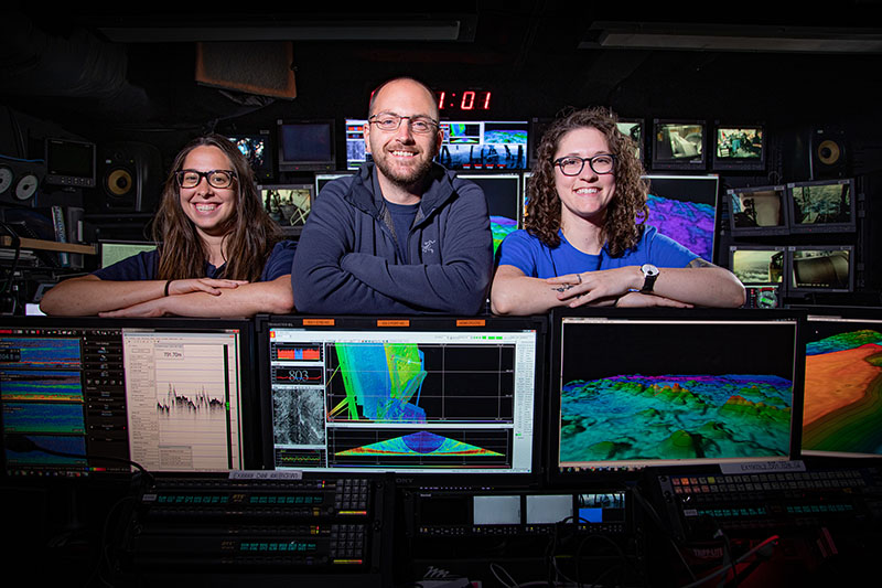 Two women and a man smiling for a picture in the control room of NOAA Ship Okeanos Explorer.