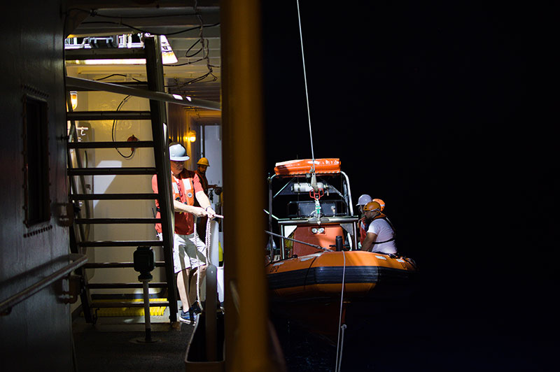 Crewmember Sidney Dunn secures a line during small boat recovery at night during the 2022 Caribbean Mapping expedition as the operations team waits to disembark.