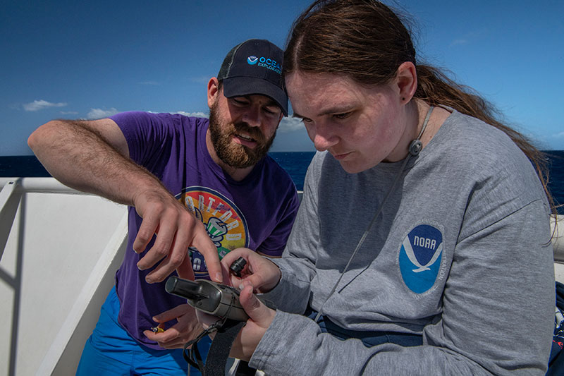 Thomas Morrow, expedition coordinator for the 2022 Caribbean Mapping expedition, works with Explorer-in-Training Kathrin Bayer to collect sun photometer measurements in support of a NASA-led, long-term research effort that assesses marine aerosols.