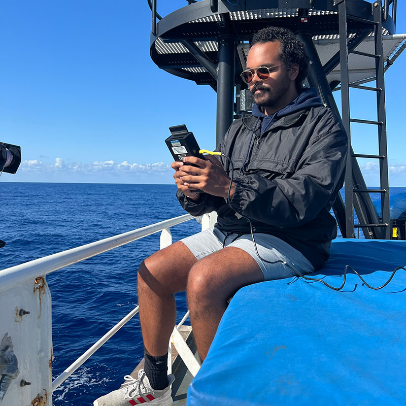 While most of our time on NOAA Ship Okeanos Explorer is spent studying what's beneath the surface of the ocean, sometimes what's above it interests us, too. In support of a NASA-led project, Treyson Gillespie uses a sunphotometer, a type of light meter, to measure maritime aerosols during the 2022 Puerto Rico Mapping and Deep-Sea Camera Demonstration. These tiny solid and liquid particles are suspended in the atmosphere above the ocean (e.g., windblown dust, sea salts, volcanic ash, smoke from fires, and pollution) and are important to scientists because they can affect climate, weather, and people's health.