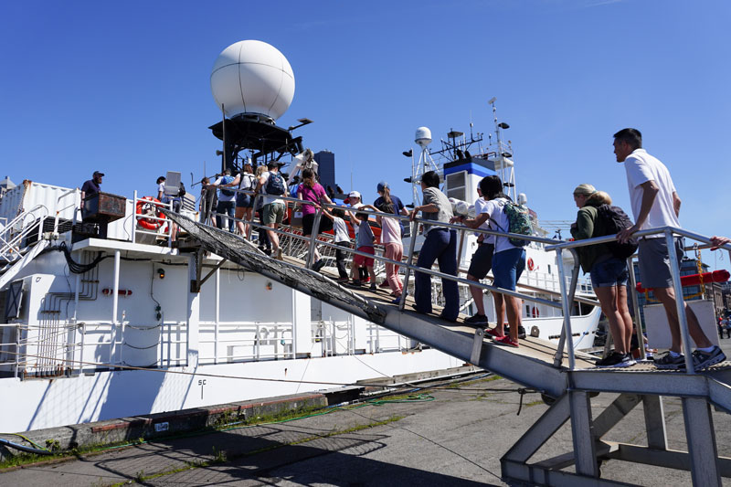 Members of the general public file up the gangplank of NOAA Ship Okeanos Explorer during the port event that took place in Seattle, Washington, following the end of the 2023 Shakedown + EXPRESS West Coast Exploration expedition. During external tours, visitors were able to get up close to remotely operated vehicles Deep Discoverer and Seirios and learn about the many technologies that are used to explore the deep ocean.