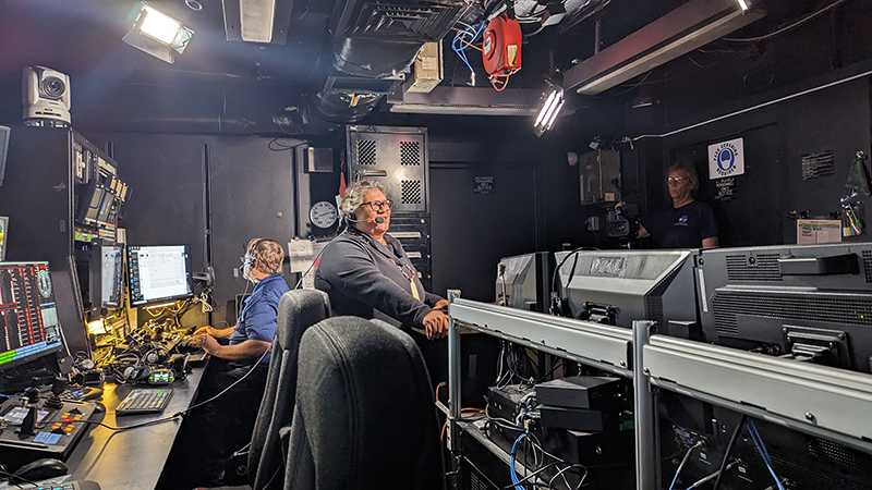 Mia Lopez in the control room of NOAA Ship Okeanos Explorer preparing to kick off a week of livestream events with the Global Foundation for Ocean Exploration’s Roland Brian (left) and Art Howard (right) in the background.