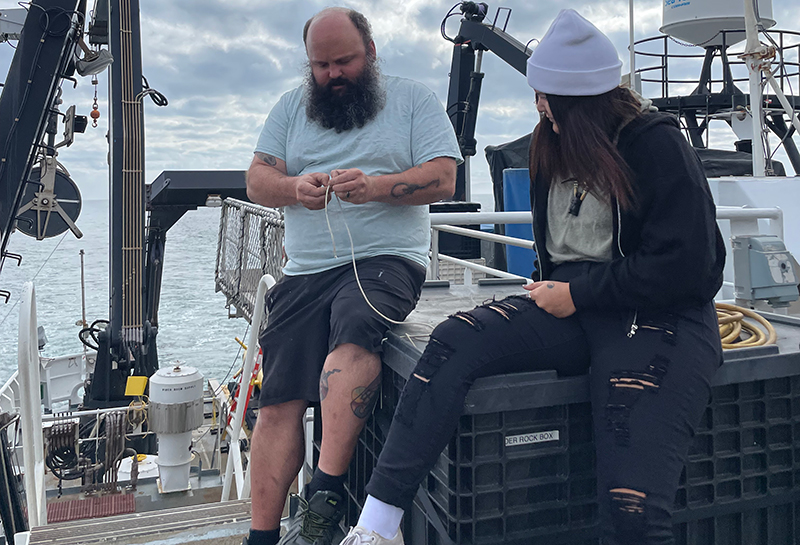 Peter Brill, an able seaman on NOAA Ship Okeanos Explorer, teaches Keli Lopez how to make nautical knots on the ship's deck.