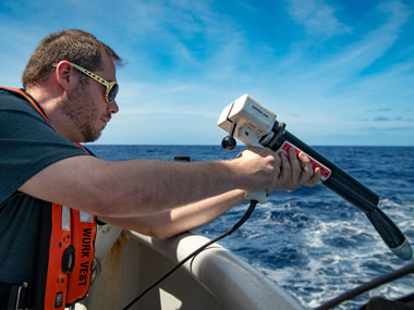 Beyond the Blue: Hawai‘i Mapping expedition coordinator Sam Cuellar prepares to conduct an expendable bathythermograph, or "XBT" for short, cast from NOAA Ship Okeanos Explorer. An XBT is a small probe that collects temperature data about the water column and, when combined with historical salinity profiles, allows the mapping team to generate sound velocity profiles that can be applied to multibeam soundings in real time for an accurate measure of bathymetry.