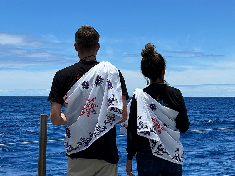 Image of cultural liaisons Makoa and Malia on the fantail looking back at Pō (night).