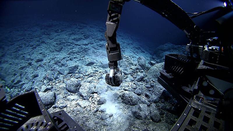 An underwater robotic arm collects a rock from a rocky sea floor.
