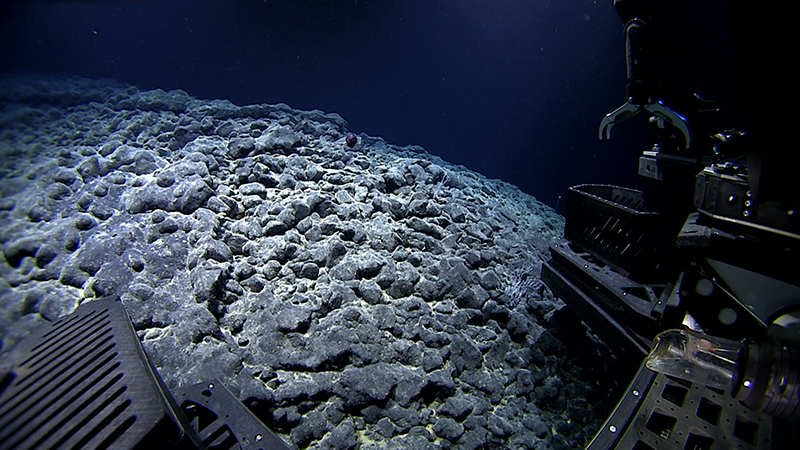 Underwater view of a rocky seabed with a submersible vehicle arm.