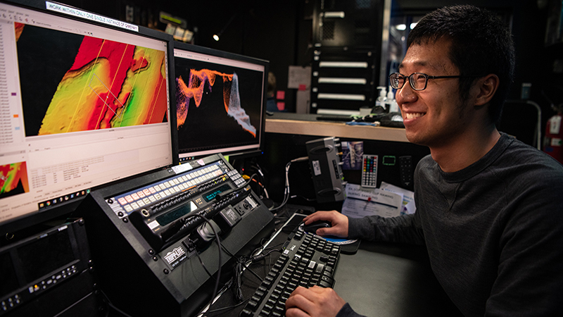 A man working at a workstation with colorful data visualizations on computer screens.