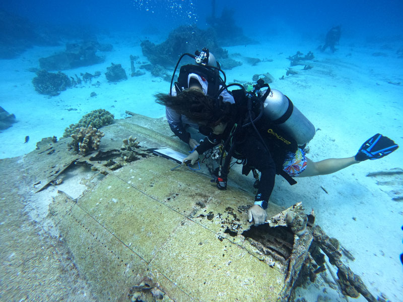Divers measuring corrosion on the aluminum wing of a H8K Kawanishi Japanese seaplane, code named "Emily," in the waters off Saipan in the Northern Mariana Islands during the Exploring Deepwater World War II Battlefields in the Pacific Using Emerging Technologies expedition.