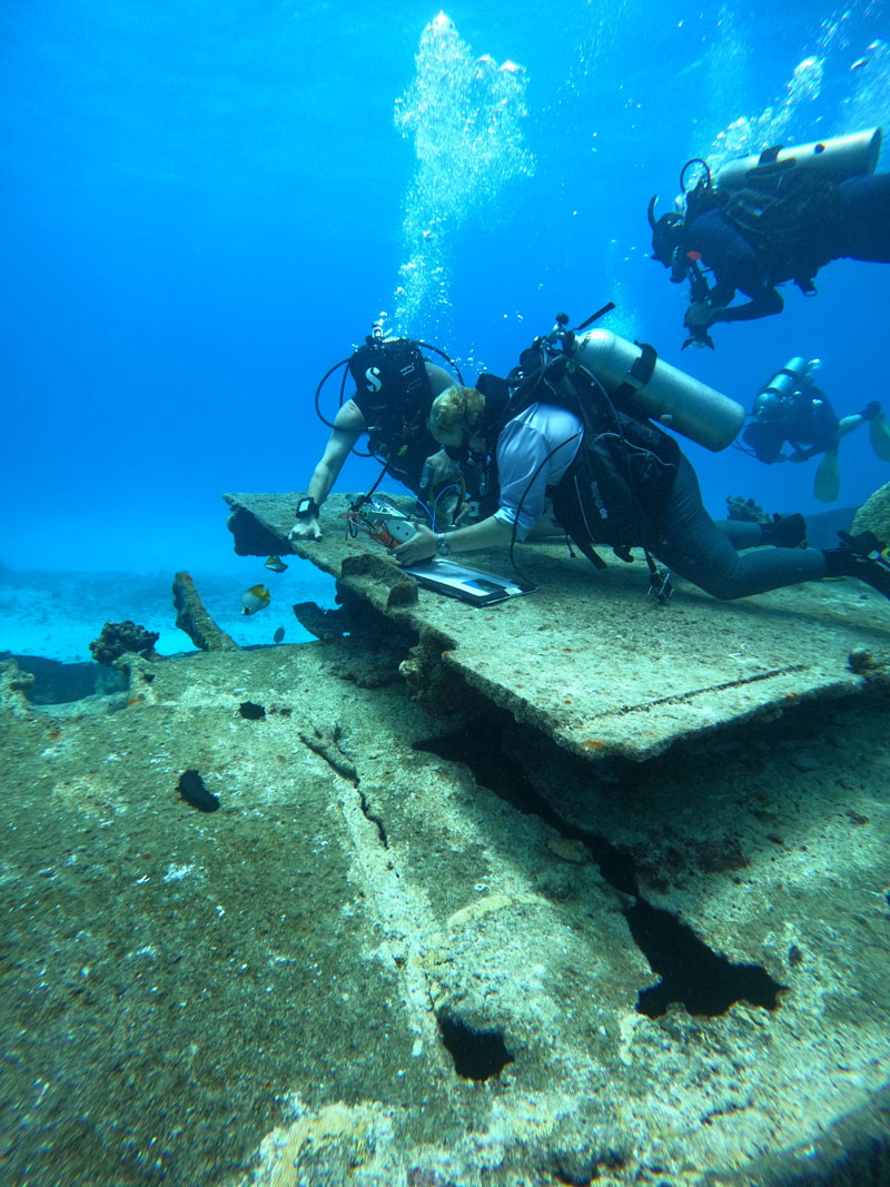 Divers using a small drill to measure corrosion on the wreck of the Japanese freighter Shoan Maru in the waters off Saipan in the Northern Mariana Islands during the Exploring Deepwater World War II Battlefields in the Pacific Using Emerging Technologies expedition.