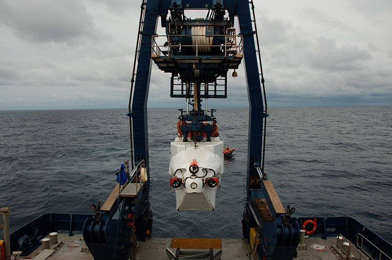 înotătorii Todd Litke și Drew Bewley stau deasupra lui Alvin în timp ce este coborât din cadrul A în apă. Odată ajunși în apă, înotătorii sunt responsabili pentru deconectarea liniilor și comunicarea cu pilotul din interior pentru a se asigura că submarinul este pregătit pentru coborâre. Pentru imagine, multumim Deep SEARCH 2018-BOEM, USGS, NOAA.