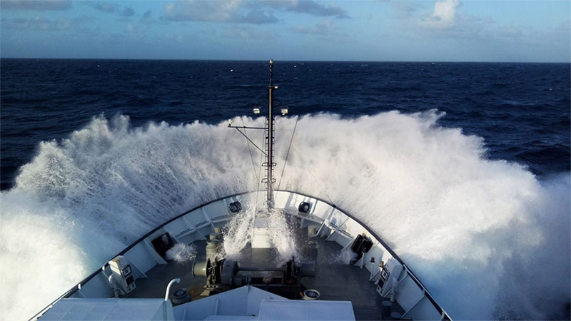 The bow of R/V Falkor slams down into moderate swell while transiting north of the equator between Samoa and Hawaii. The swell in this part of the ocean is known to be heavy due to the constant trade winds that blow at about 25 knots in this region. Image courtesy of Schmidt Ocean Institute/Cherie Colyer-Morris.
